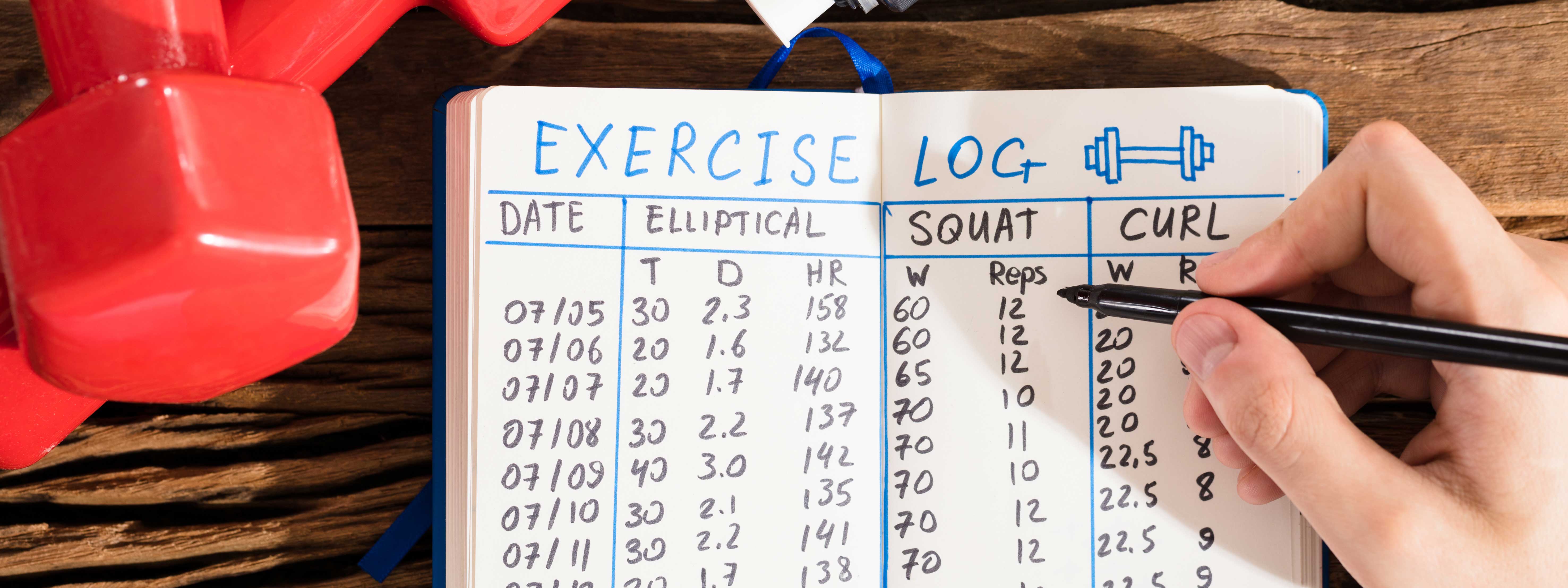 Hand holding a pen filling our a workout log book